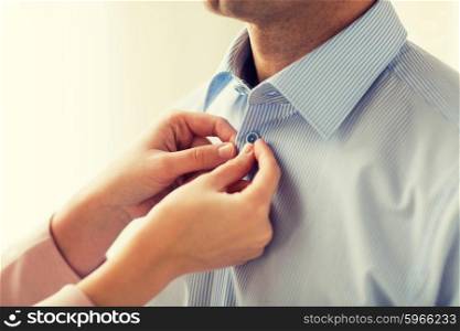 people, business, care and clothing concept - close up of woman helping man and fastening buttons on his shirt at home