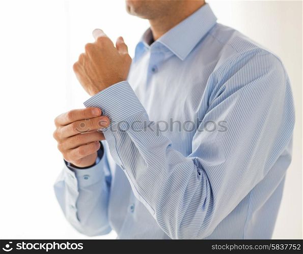 people, business, fashion and clothing concept - close up of man fastening buttons on shirt sleeve at home