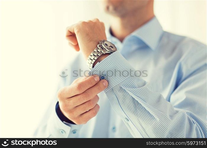 people, business, fashion and clothing concept - close up of man fastening buttons on shirt sleeve at home