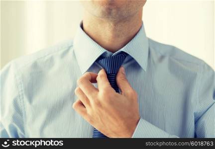 people, business, fashion and clothing concept - close up of man in shirt dressing up and adjusting tie on neck at home