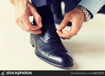 people, business, fashion and footwear concept - close up of man leg and hands tying shoe laces