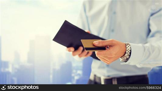 people, business, finances and money concept - close up of businessman hands holding open wallet and credit card over city background
