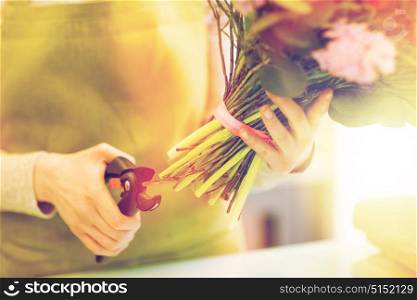 people, business, sale and floristry concept - close up of florist woman making bunch and cropping stems by pruner at flower shop. close up of florist woman with flowers and pruner