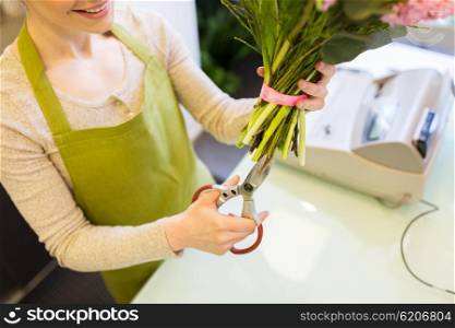 people, business, sale and floristry concept - close up of florist woman making bunch and cropping stems by scissors at flower shop