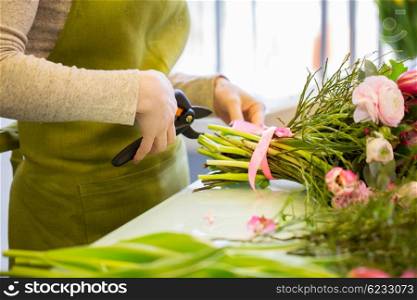 people, business, sale and floristry concept - close up of florist woman making bunch and cropping stems by pruner at flower shop