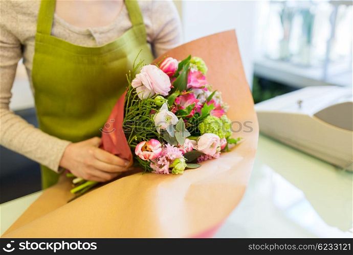 people, business, sale and floristry concept - close up of florist woman wrapping bunch into paper at flower shop