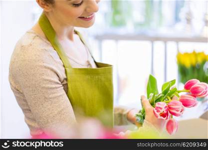people, business, sale and floristry concept - close up of happy florist woman making tulip bunch at flower shop
