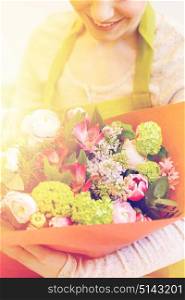people, business, sale and floristry concept - close up of happy smiling florist woman holding bunch of flowers wrapped into paper at flower shop. close up of woman with bunch at flower shop
