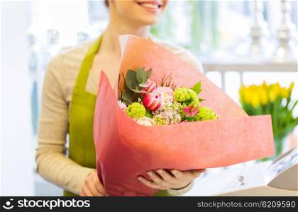 people, business, sale and floristry concept - close up of happy smiling florist woman holding bunch of flowers wrapped into paper at flower shop