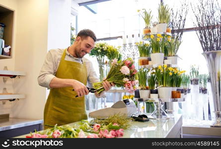 people, business, sale and floristry concept - happy smiling florist man making bunch and cropping stems by scissors at flower shop