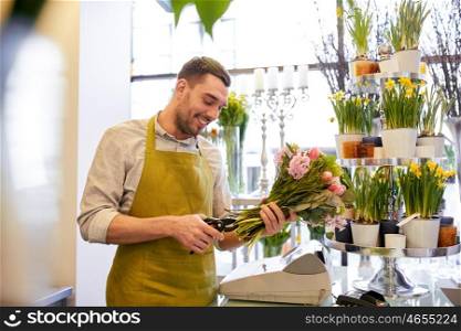 people, business, sale and floristry concept - happy smiling florist man making bunch and cropping stems by scissors at flower shop