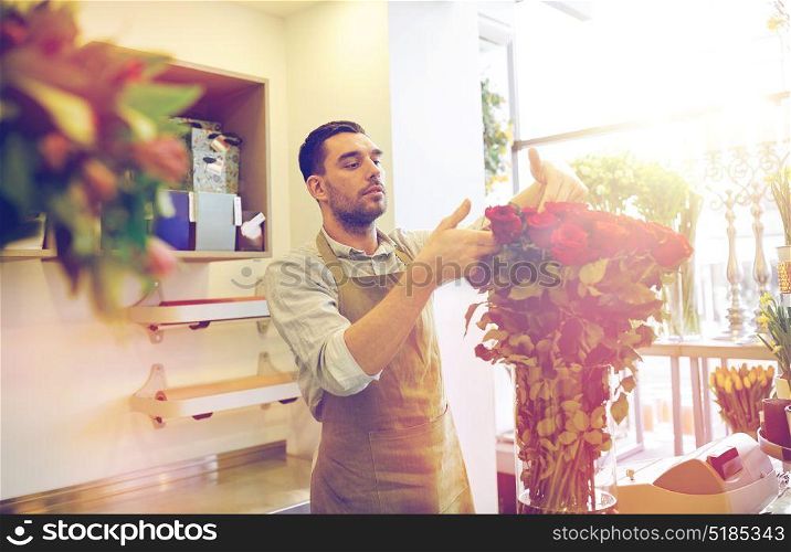 people, business, sale and floristry concept - happy smiling florist man with red roses at flower shop. smiling florist man with roses at flower shop