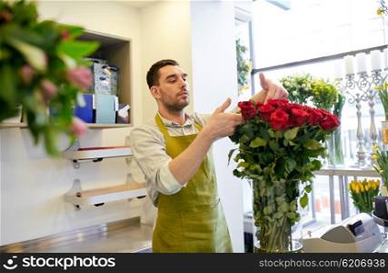 people, business, sale and floristry concept - happy smiling florist man with red roses at flower shop