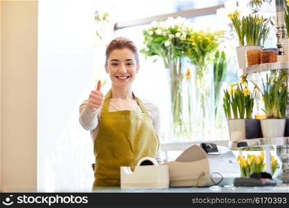 people, business, sale and floristry concept - happy smiling florist woman at flower shop cashbox showing thumbs up