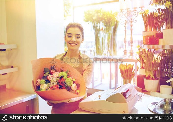 people, business, sale and floristry concept - happy smiling florist woman holding bunch of flowers wrapped into paper at flower shop. smiling florist woman with bunch at flower shop