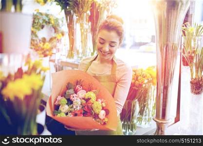 people, business, sale and floristry concept - happy smiling florist woman holding bunch of flowers wrapped into paper at flower shop. smiling florist woman with bunch at flower shop