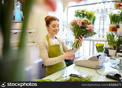 people, business, sale and floristry concept - happy smiling florist woman making bunch and cropping stems by scissors at flower shop