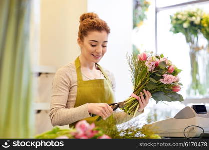 people, business, sale and floristry concept - happy smiling florist woman making bunch and cropping stems by scissors at flower shop