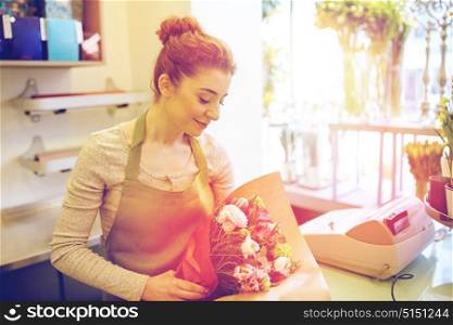 people, business, sale and floristry concept - happy smiling florist woman wrapping bunch into paper at flower shop. smiling florist woman packing bunch at flower shop