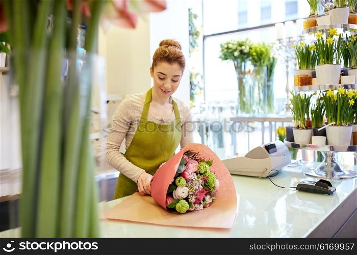 people, business, sale and floristry concept - happy smiling florist woman wrapping bunch into paper at flower shop