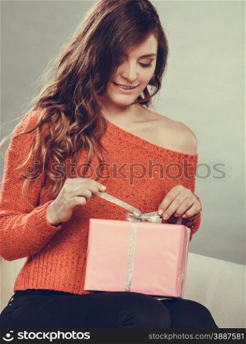 People celebrating xmas love and happiness concept - beauty girl opening present pink gift box sitting on sofa at home