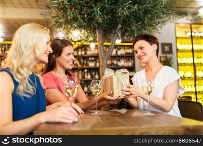people, celebration and greeting concept - happy women giving birthday present to friend at wine bar or restaurant. women giving present to friend at wine bar