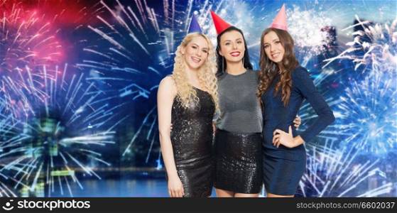 people, celebration and holidays concept - happy women with party caps hugging over firework lights background. happy women with party caps over firework