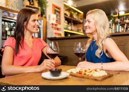 people, celebration and lifestyle concept - happy women drinking red wine and talking at restaurant or bar. happy women drinking red wine at bar or restaurant