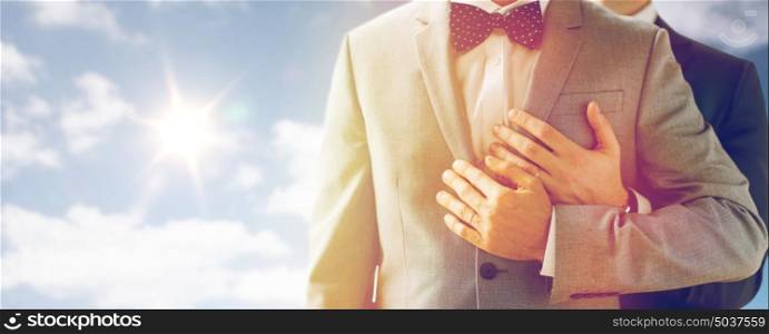 people, celebration, homosexuality, same-sex marriage and love concept - close up of happy male gay couple with wedding rings hugging over sky and sun background. close up of male gay couple with wedding rings on