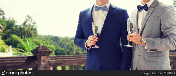 people, celebration, homosexuality, same-sex marriage and love concept - close up of happy married male gay couple drinking sparkling wine from glasses on wedding over balcony and nature background