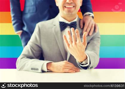 people, celebration, homosexuality, same-sex marriage and love concept - close up of male gay couple with wedding rings on putting hand on shoulder over rainbow flag background