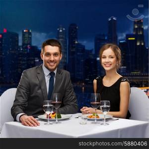 people, celebration, romantic and holidays concept - smiling couple eating main course with red wine at restaurant over night city background