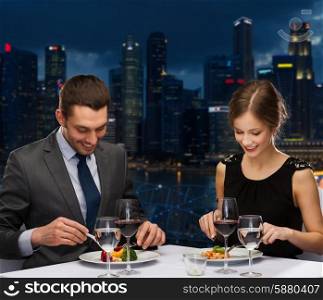 people, celebration, romantic and holidays concept - smiling couple eating main course with red wine at restaurant over night city background