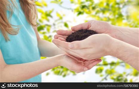 people, charity, family and legacy concept - close up of father and girl holding soil in cupped hands over green nature background