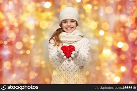 people, charity, holidays, children and love concept - smiling teenage girl in winter clothes with small red heart over lights background