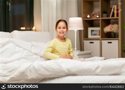 people, childhood and bedtime concept - happy little girl in bed at home bedroom at night. happy little girl in bed at home at night