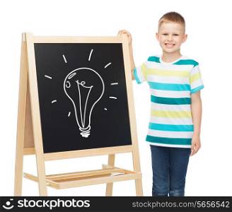 people, childhood and education concept - smiling little boy with bulb drawing on blackboard over white background