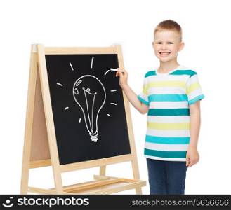 people, childhood and education concept - smiling little boy with bulb drawing on blackboard over white background