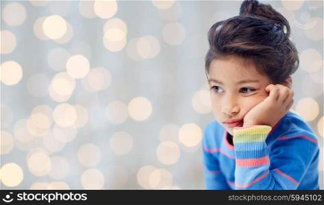 people, childhood and emotions concept - sad and disappointed or bored little girl over holidays lights background