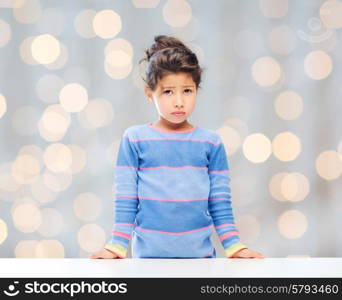 people, childhood and emotions concept - sad little girl over holidays lights background