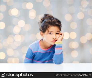people, childhood and emotions concept - sad little girl over holidays lights background
