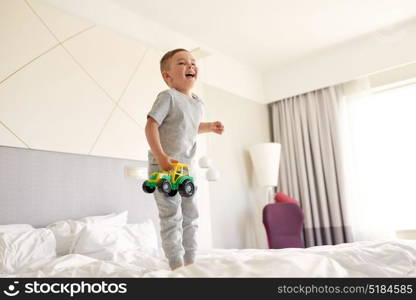 people, childhood and morning concept - happy little boy with toy car on home or hotel bed. happy little boy with toy car on home or hotel bed