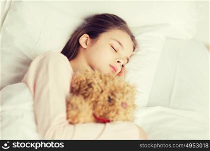 people, childhood, rest and comfort concept - girl sleeping with teddy bear toy in bed at home. girl sleeping with teddy bear toy in bed at home