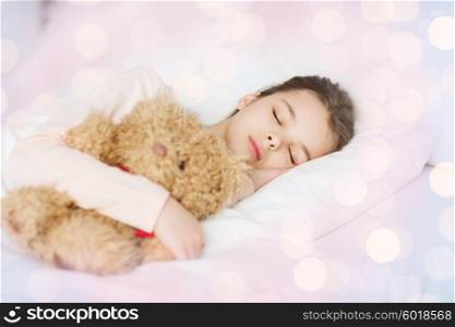 people, childhood, rest and comfort concept - girl sleeping with teddy bear toy in bed over lights