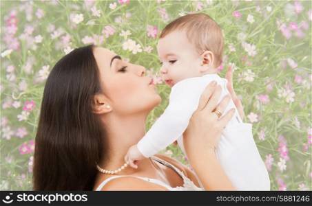 people, childhood, royalty and happiness concept - happy mother kissing and holding baby over floral background