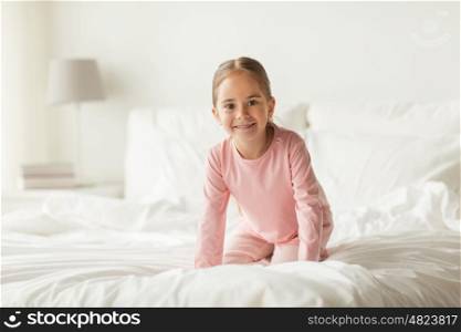people, children and bedtime concept - happy little girl on bed at home bedroom