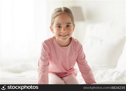 people, children and bedtime concept - happy little girl on bed at home bedroom