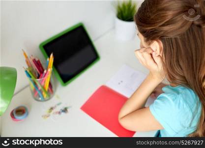 people, children and education concept - girl with tablet pc computer writing to notebook at home. girl with tablet pc writing to notebook at home