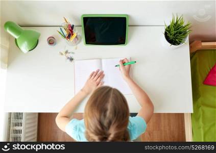 people, children and education concept - girl with tablet pc computer writing to notebook at home. girl with tablet pc writing to notebook at home