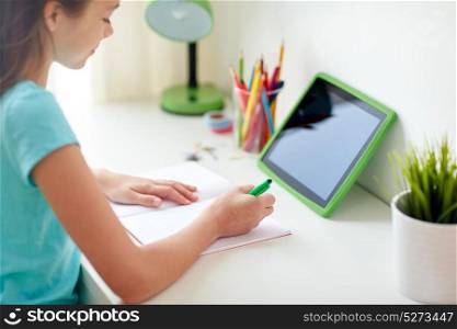 people, children and education concept - happy girl with tablet pc computer writing to notebook at home. girl with tablet pc writing to notebook at home